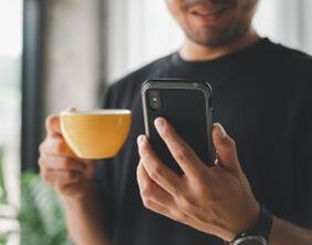 Man holding a mug and cell phone. マグを片手に携帯を見ている男性。