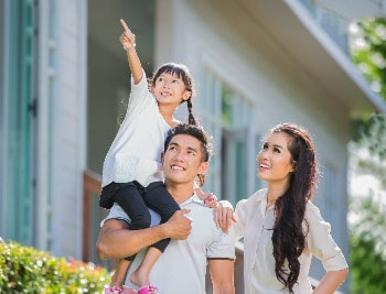 Asian family with a girl on her father's shoulder pointing her finger up and everyone is looking up in front of their house. 