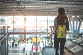 A long-haired woman with a yellow backpack and a silver suitcase is looking over the crowd in the airport.