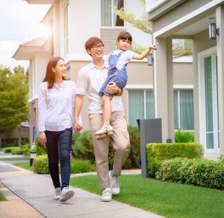 An asian family of 3 is walking on the path by a row of modern homes. 