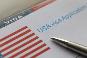 Close-up of a form 'USA visa application' with a U.S. flag image on the left. A silver pen is placed on the form.